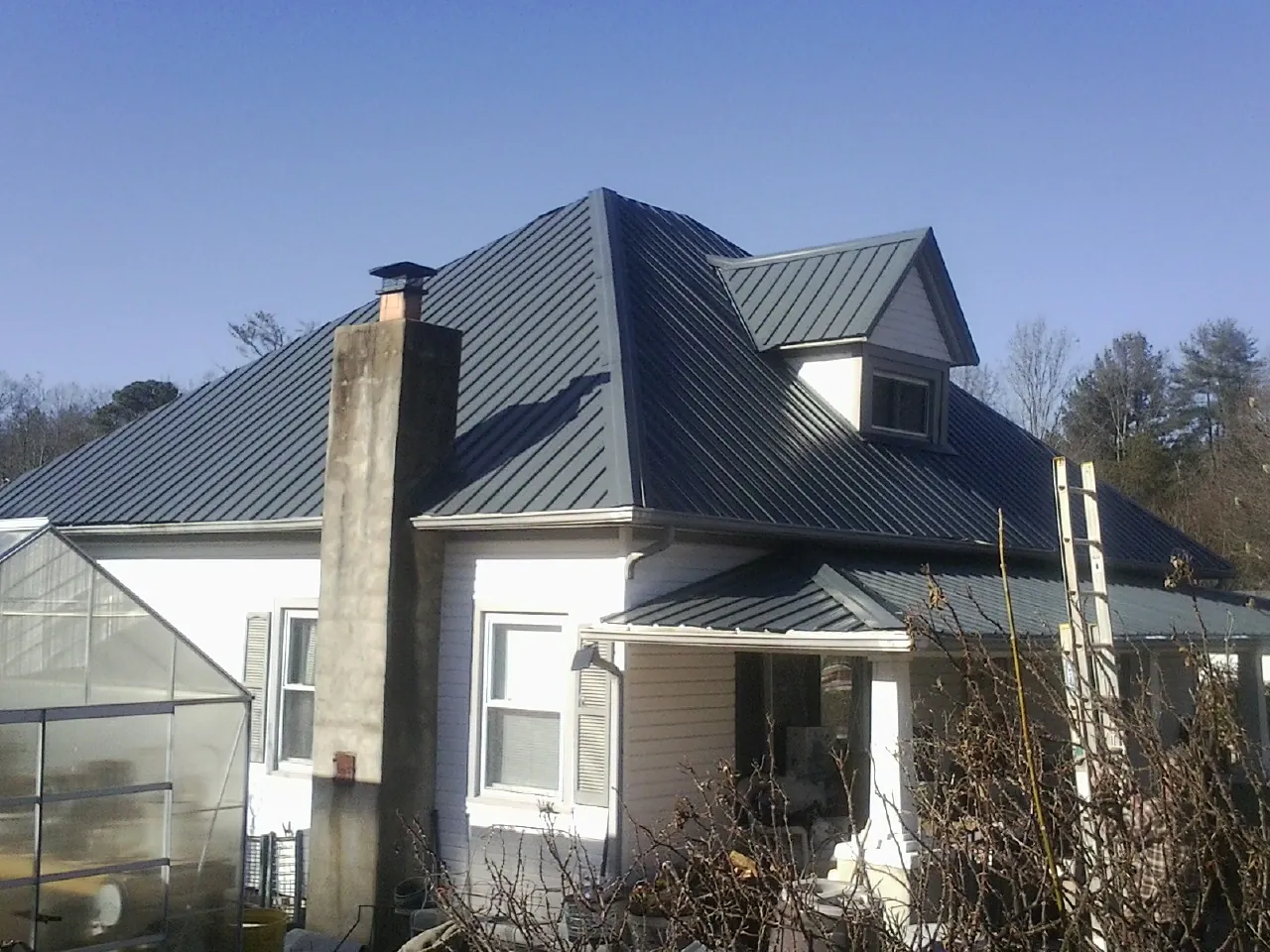 Dark blue standing seam metal roof on a white farmhouse with dormer — Slate & Tile Roof Repair by Roofing Brothers in Puryear