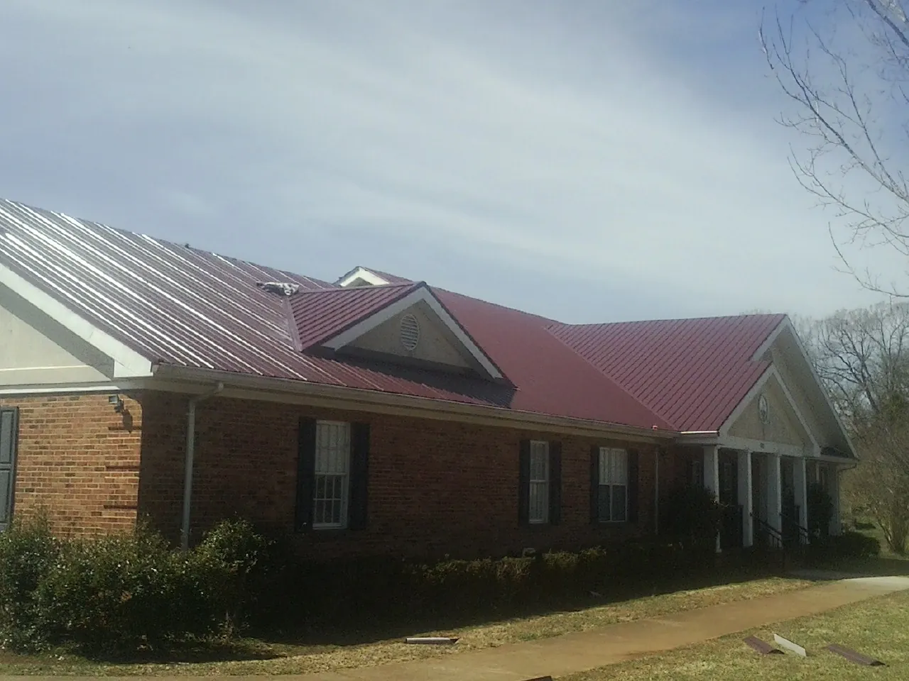 Red metal roof with gabled entries on a long brick building, from a Hail Damage Roof Repair job in Puryear