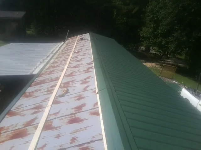 Old rusted panels beside newly installed green metal roofing — Wind Damage Roof Repair by Roofing Brothers in Puryear