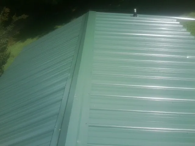 New green metal panels meeting at the ridge of a roof — Flat Roof Repair work by our crew in Puryear