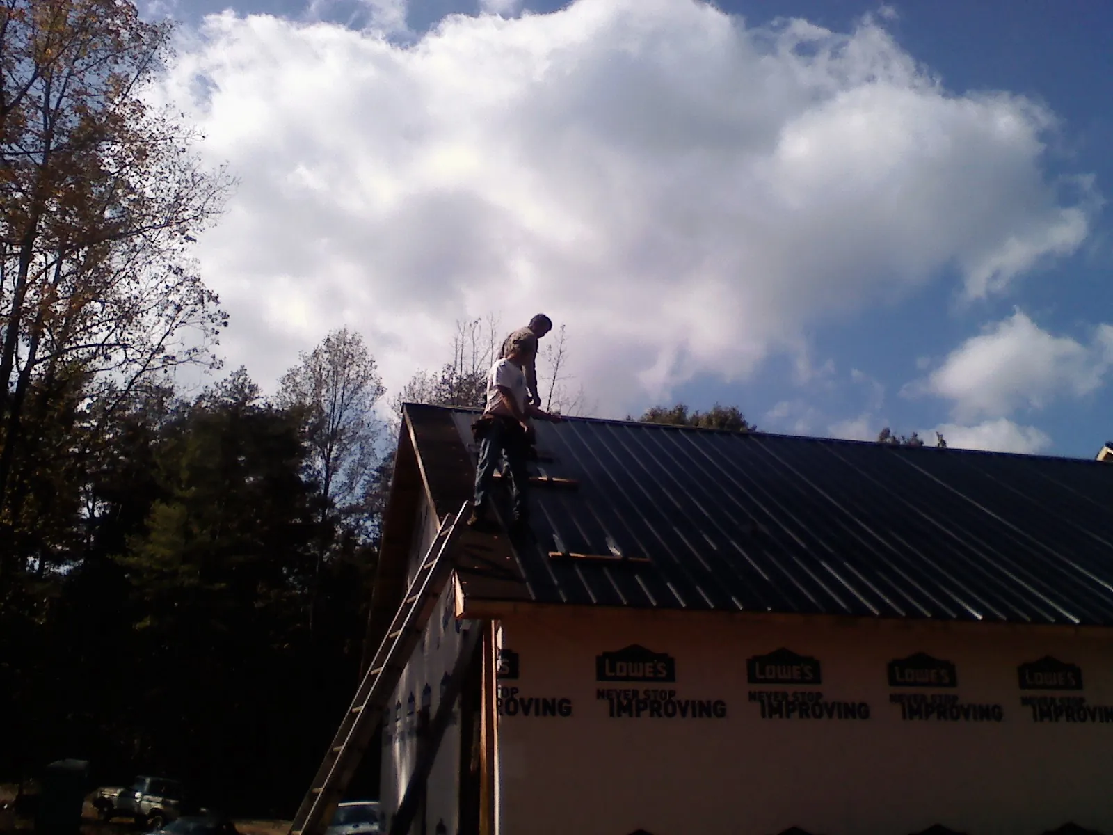 Roofer fastening dark metal panels high against a cloudy sky, from a Roof Inspection job in Puryear