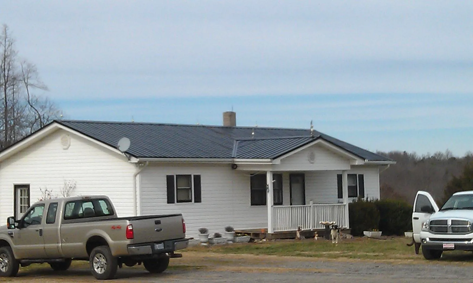 Finished dark metal roof on a white ranch home with work trucks parked in Puryear