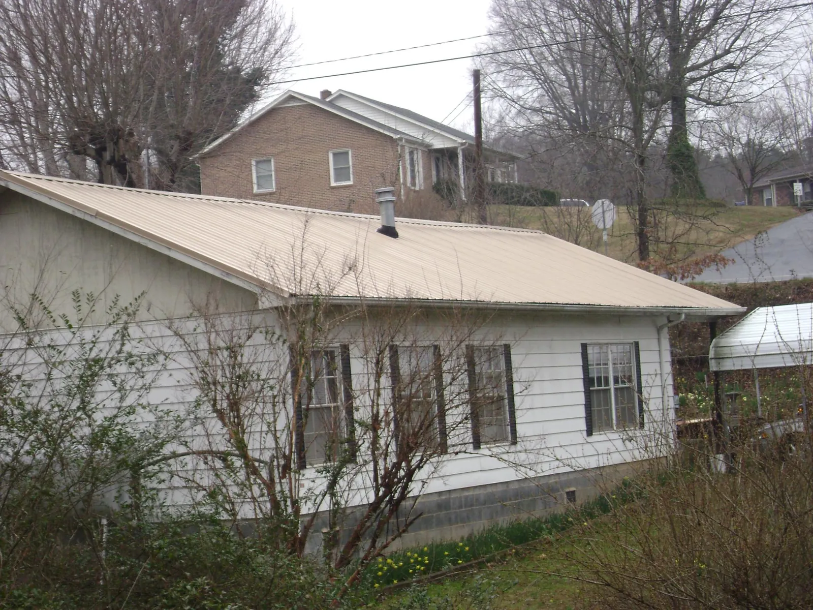 Tan metal roof on a white sided house set into a hillside — Commercial Roofing by Roofing Brothers in Puryear