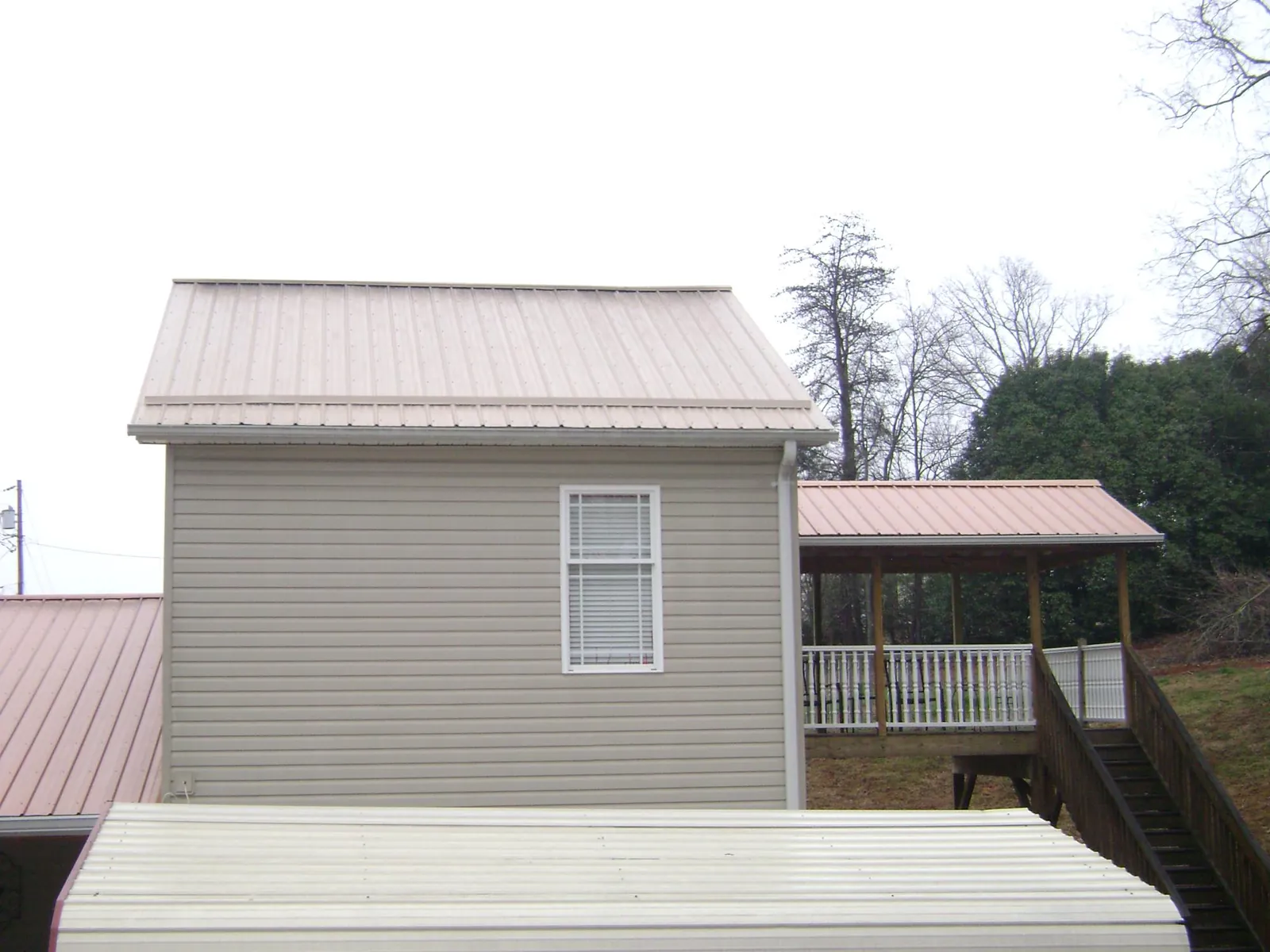 Tan metal roofs on a two story addition and attached porch, from a Roof Replacement job in Puryear